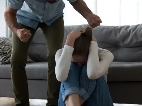 Frightened scared young defenseless woman victim hiding from aggressive man suffer from physical abuse, abusive husband threaten beat upset crying wife with fists, fear of domestic violence concept