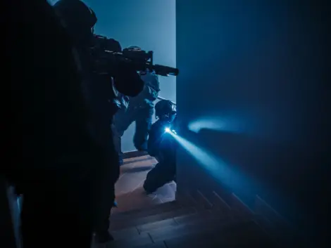 Masked Squad of Armed SWAT Police Officers Move Up the Stairs in a Corridor of an Office Building. Soldiers with Rifles and Flashlights Move Forwards and Cover Surroundings.